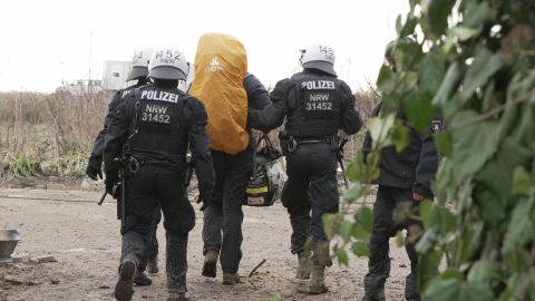 Three police officers escort an activist from the Lützerath site.